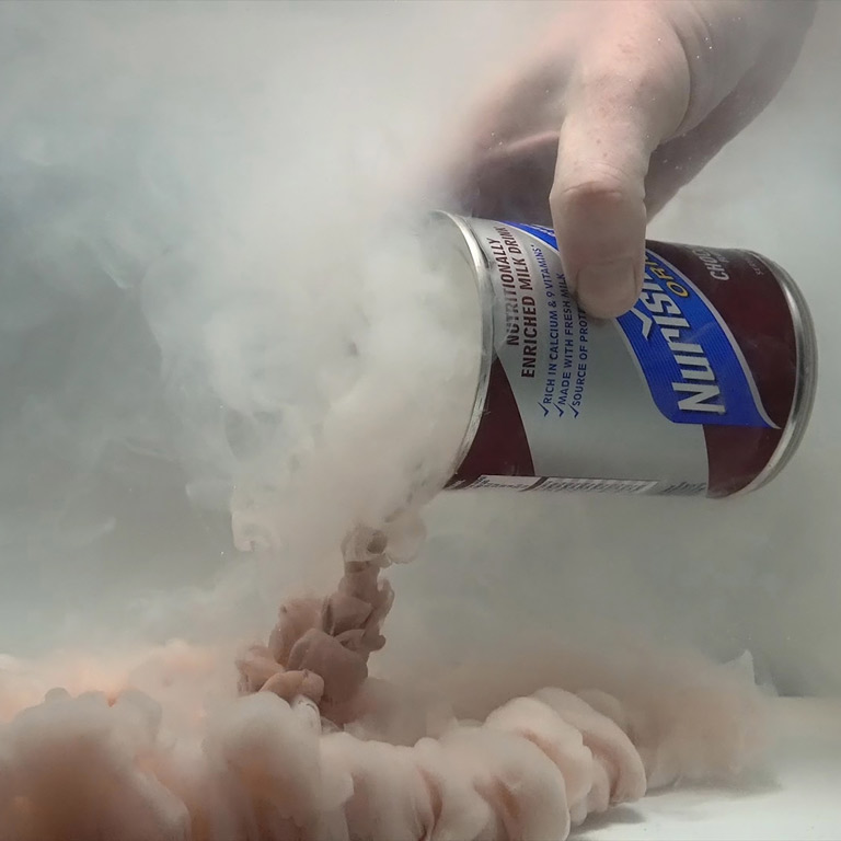 A person pours an open can of a brownish substance under water.